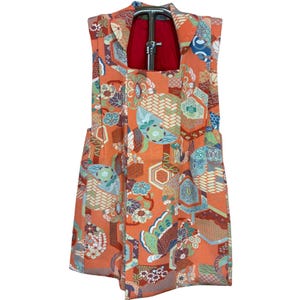 May include: A sleeveless orange garment with a colorful floral and geometric pattern. The design incorporates shades of blue, green, and brown. The garment is displayed on a hanger.