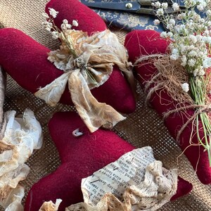 May include: Burgundy fabric heart decorations with cream lace and ribbon details. Some hearts are decorated with dried baby's breath and twine. Vintage scissors are visible in the background.