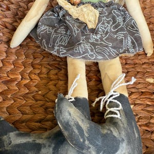 Puede incluir: Mu&ntilde;eca de tela hecha a mano con un delantal verde, una falda con estampado de animales de granja y botas negras con cordones blancos. La mu&ntilde;eca tiene brazos y piernas de color beige y cabeza y torso beige.