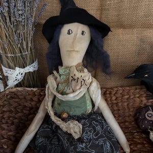 Puede incluir: Mu&ntilde;eca de tela hecha a mano vestida de bruja, con sombrero negro y falda oscura con estampado de animales blancos. La mu&ntilde;eca tiene pelo azul y una parte superior verde. Un art&iacute;culo decorativo con tem&aacute;tica de Halloween o oto&ntilde;o.