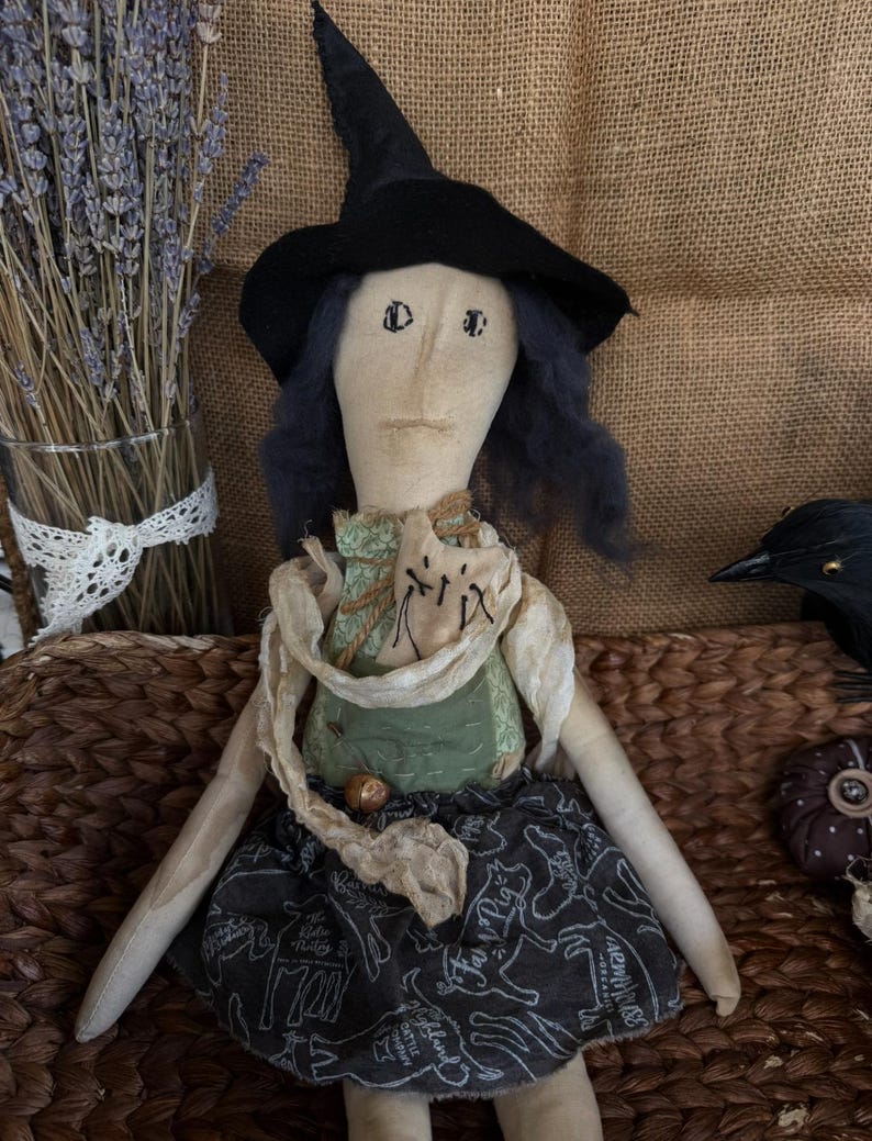 Puede incluir: Mu&ntilde;eca de tela hecha a mano vestida de bruja, con sombrero negro y falda oscura con estampado de animales blancos. La mu&ntilde;eca tiene pelo azul y una parte superior verde. Un art&iacute;culo decorativo con tem&aacute;tica de Halloween o oto&ntilde;o.