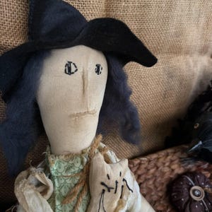 Puede incluir: Mu&ntilde;eca de bruja hecha a mano con sombrero negro y pelo azul. La mu&ntilde;eca lleva un vestido verde y un chal color crema. Una peque&ntilde;a bolsa con forma de gato est&aacute; sujeta al pecho de la mu&ntilde;eca. La mu&ntilde;eca forma parte de una colecci&oacute;n tem&aacute;tica de Halloween o oto&ntilde;o.