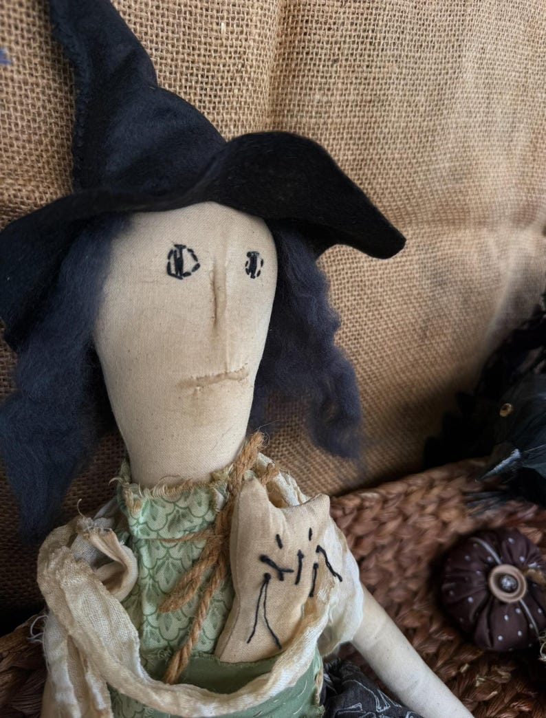 Puede incluir: Mu&ntilde;eca de bruja hecha a mano con sombrero negro y pelo azul. La mu&ntilde;eca lleva un vestido verde y un chal color crema. Una peque&ntilde;a bolsa con forma de gato est&aacute; sujeta al pecho de la mu&ntilde;eca. La mu&ntilde;eca forma parte de una colecci&oacute;n tem&aacute;tica de Halloween o oto&ntilde;o.