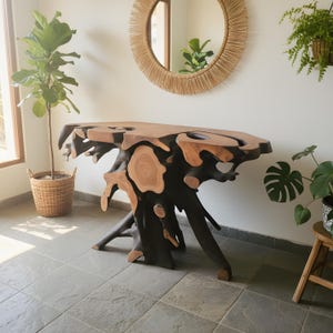 May include: A distinctive console table crafted from natural wood. The table has a dark, textured base and a light brown, organically shaped top. The design highlights the natural form of the wood, creating a striking, artistic piece for home decor.