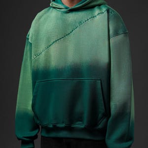Puede incluir: Sudadera con capucha verde degradado con bolsillo de canguro y costura diagonal cosida en el pecho. La sudadera con capucha tiene una capucha con cord&oacute;n y mangas largas. El color pasa de un verde m&aacute;s claro en la parte superior a un verde m&aacute;s oscuro en la parte inferior.