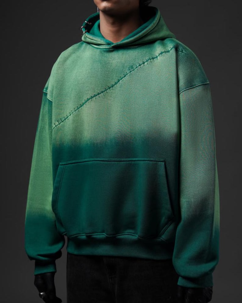 Puede incluir: Sudadera con capucha verde degradado con bolsillo de canguro y costura diagonal cosida en el pecho. La sudadera con capucha tiene una capucha con cord&oacute;n y mangas largas. El color pasa de un verde m&aacute;s claro en la parte superior a un verde m&aacute;s oscuro en la parte inferior.