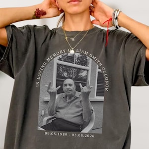 May include: Pepper-coloured t-shirt with a black and white photo of a man, text reading "IN LOVING MEMORY OF LIAM SMITH O'CONNOR" and dates "09.05.1989 - 03.08.2026". The shirt has a relaxed fit.