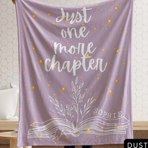 May include: Dusty purple throw blanket with the text "Just one more chapter" in white script. The blanket features a floral design and the name "Sophie". Gold star accents are scattered across the blanket.