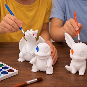 May include: Three white unpainted ceramic figurines of cartoon creatures, including a dragon, a turtle, and a rabbit. The figures are being painted with blue and orange brushes, with one eye on each figure already colored in red, blue, or orange.