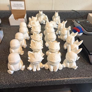 May include: A collection of small, unpainted white 3D-printed figurines depicting various creatures. The set includes multiple figures of characters with distinct features such as pointed ears, rounded bodies, and tails, arranged in rows.