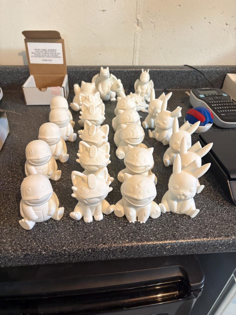 May include: A collection of small, unpainted white 3D-printed figurines depicting various creatures. The set includes multiple figures of characters with distinct features such as pointed ears, rounded bodies, and tails, arranged in rows.
