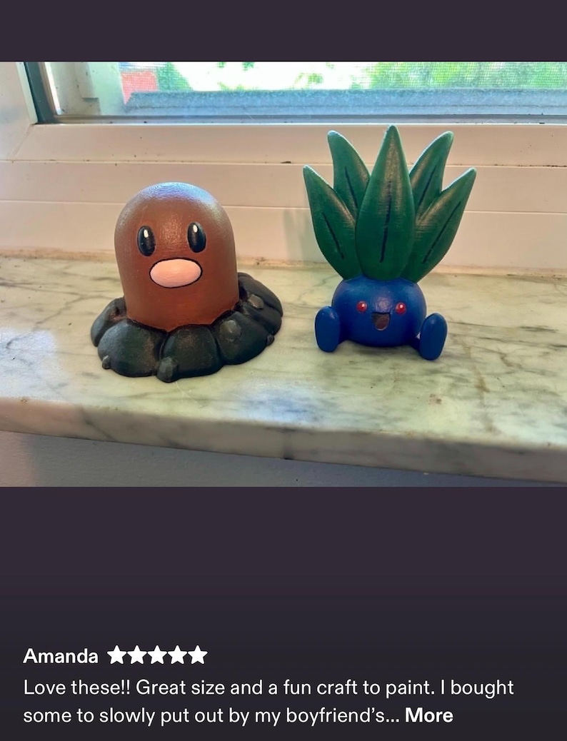 May include: Two small figurines, one brown, cylindrical creature with a pink nose and black eyes, and one blue, round creature with green, leaf-like protrusions on top, red eyes, and a small open mouth, both displayed as decorative items.