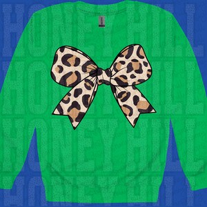 May include: A green sweatshirt with a large leopard print bow in brown and black. The bow is the central design element on the front of the long-sleeved top. The brand name "Honey Hill" is visible in the background.