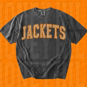 May include: A charcoal grey short-sleeve t-shirt with a crew neckline. The front features the word JACKETS in a large, arched, collegiate-style font. The letters are white with thin vertical orange stripes and a bold orange outline.