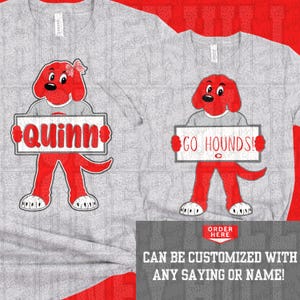Può includere: Una t-shirt grigio melange con la grafica di un cane rosso in stile cartoon. Il cane a sinistra indossa un fiocco e tiene un cartello con scritto Quinn. Il cane a destra tiene un cartello con GO HOUNDS!. Il testo indica la possibilità di personalizzare.