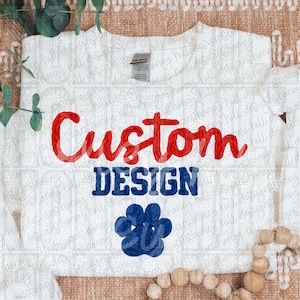 May include: White t-shirt with the words "Custom Design" in red and blue. A blue paw print design is below the text. The shirt is made of a soft material.