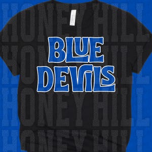 May include: A black short-sleeved t-shirt featuring the text "BLUE DEVILS" printed in a bold, blue font with a white outline across the chest. The shirt has a standard crew neckline and a white brand label attached to the inside of the collar.