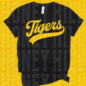 Op de afbeelding: Een zwart T-shirt met korte mouwen en het woord Tigers in een groot, vet, geel cursief lettertype op de borst. Het shirt heeft een ronde hals en een standaard pasvorm, met een wit merklabel zichtbaar aan de binnenkant van de kraag.