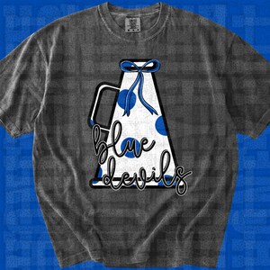 Peut inclure: Un t-shirt gris anthracite à manches courtes orné d'un motif de mégaphone blanc à pois bleus avec un nœud ruban bleu. Le mégaphone porte l'inscription blue devils écrite en lettres cursives noires au centre du motif graphique.