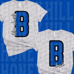 May include: Two light gray short-sleeve t-shirts. The top shirt features a large blue letter B with a black outline and the text blue devils. The bottom shirt features a large blue letter B with a black outline and the text bush.