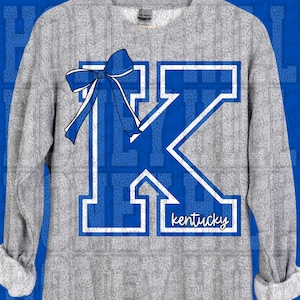 以下が含まれることがあります： グレーのスウェットシャツ。大きな青色の「K」のデザインに白い縁取りと青いリボンが施されています。「kentucky」の文字が下に書かれています。長袖のスウェットシャツにプリントされたデザインで、肌寒い日に最適です。