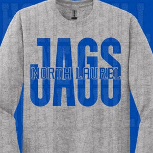 Puede incluir: Una sudadera gris jaspeada con la palabra "JAGS" en letras azules grandes. Debajo, el texto "NORTH LAUREL" también en azul. La sudadera tiene cuello redondo y mangas largas.