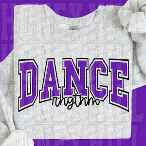 May include: A white long-sleeved shirt with the word "DANCE" in large purple block letters outlined in black. Below the word "DANCE" is the word "rhythm" in a cursive font. The shirt is a crew neck style.
