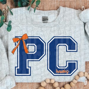 May include: A light gray sweatshirt featuring the letters "PC" in blue with a white outline and a bow. The letters have a striped pattern. The word "hawks" is in orange at the bottom of the "C".