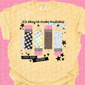 May include: A pale yellow t-shirt featuring a graphic of four pencils with different patterns including black and white buffalo plaid, green and yellow gingham, leopard print, and blue stars. The text reads it's okay to make mistakes JUST KEEP GOING.