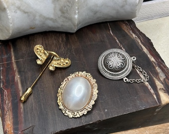 Trío de broches vintage: broche de barra dorado, cabujón color crema, broche de cadena con medallón plateado
