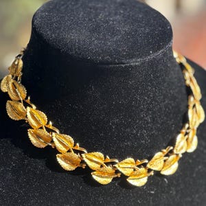 Könnte beinhalten: Eine goldfarbene Halskette mit Blattmuster. Die Halskette wird auf einer schwarzen Samtbüste präsentiert. Die Blätter haben strukturierte Adern und sind zu einer Halskette verbunden. Der Schmuck ist wahrscheinlich Vintage.