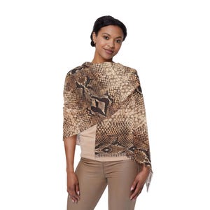 Peut inclure: Un châle à motif peau de serpent marron et beige avec une bordure à franges. Le châle est drapé sur les épaules, créant un accessoire élégant. Le motif présente un mélange de tons bruns clairs et foncés.