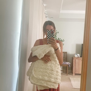 Pu&ograve; includere: Una persona tiene una coperta di uncinetto bianca davanti a uno specchio. La persona indossa una tuta rossa.