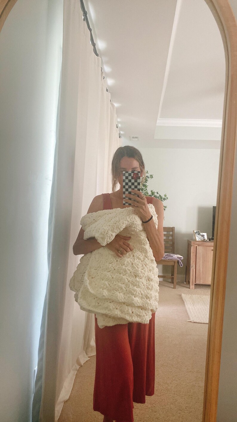 Pu&ograve; includere: Una persona tiene una coperta di uncinetto bianca davanti a uno specchio. La persona indossa una tuta rossa.