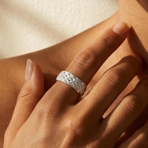 May include: A silver ring featuring a detailed, intricate woven or braided texture across its entire outer surface. The band has a consistent width and a polished metallic finish that reflects light, creating a textured appearance on the finger.