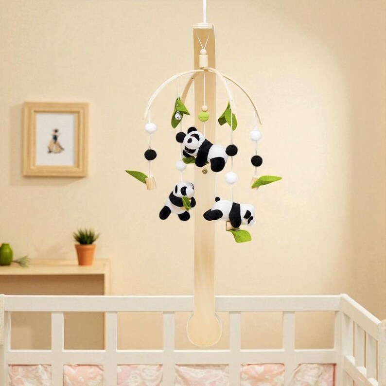 May include: A baby crib mobile featuring three plush panda bears in black and white, suspended from a wooden frame. The mobile includes green leaf accents, white and black spheres, and is designed to hang above a crib.
