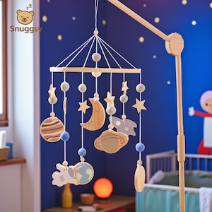Op de afbeelding: Een houten baby mobile met planeten, sterren, manen en een astronaut. De mobiel hangt aan een houten frame en heeft blauwe en grijze accenten. Het Snuggysy-logo is linksboven zichtbaar.