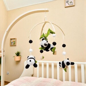 May include: A baby mobile featuring panda bear plush toys in black and white, suspended from a wooden frame. The mobile includes green leaf accents and black and white spherical ornaments, designed to hang over a crib.