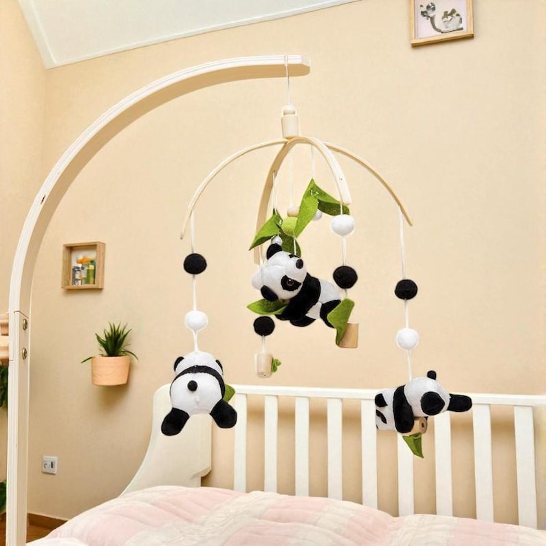 May include: A baby mobile featuring panda bear plush toys in black and white, suspended from a wooden frame. The mobile includes green leaf accents and black and white spherical ornaments, designed to hang over a crib.