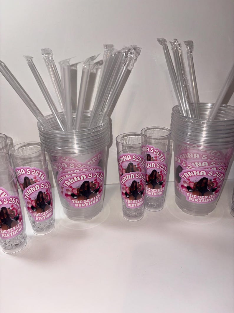 May include: Clear plastic cups and shot glasses with pink and white labels. The labels read "Yanna's 26th" and "The Sexiest Birthday" with an image of a woman. Clear plastic straws are included.