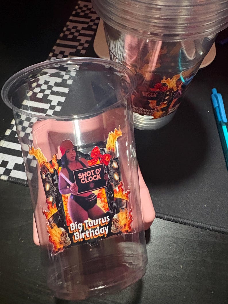 May include: Clear plastic cups with a colorful graphic. The graphic features a person holding a sign that says "Shot O' Clock" and "Big Taurus Birthday" with flames and skulls.