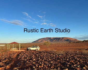 Op de afbeelding: Een landschap met een witte SUV geparkeerd bij een schuilplaats met een rood dak. De tekst "Rustic Earth Studio" wordt weergegeven tegen een blauwe lucht. Een grote berg is zichtbaar op de achtergrond.