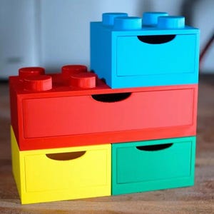 May include: A stack of four colorful storage drawers designed to resemble large toy building blocks. The drawers are in bright primary colors: red, blue, yellow, and green. Each drawer has a curved handle for easy opening and closing.