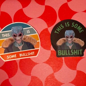 May include: Two stickers featuring an alien with blue skin and a fur collar. One sticker has a retro design with the text "THIS IS SOME BULLSHIT". The other sticker has a black background with the same alien and text.