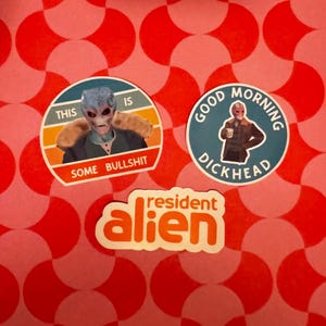 May include: Three stickers on a red and pink patterned background. One sticker features an alien with the text "THIS IS SOME BULLSHIT." Another sticker says "GOOD MORNING DICKHEAD." The third sticker says "resident alien."