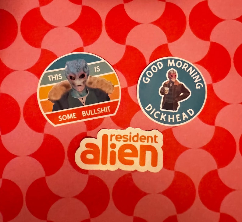 May include: Three stickers on a red and pink patterned background. One sticker features an alien with the text "THIS IS SOME BULLSHIT." Another sticker says "GOOD MORNING DICKHEAD." The third sticker says "resident alien."