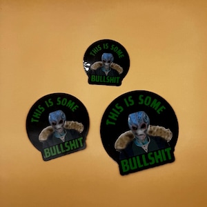 May include: Three black circular stickers with a blue-skinned alien graphic. The stickers have the text "THIS IS SOME BULLSHIT" in green. The alien has a gray face and is wearing a jacket.
