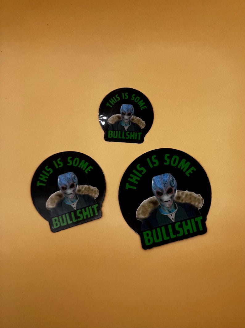 May include: Three black circular stickers with a blue-skinned alien graphic. The stickers have the text "THIS IS SOME BULLSHIT" in green. The alien has a gray face and is wearing a jacket.