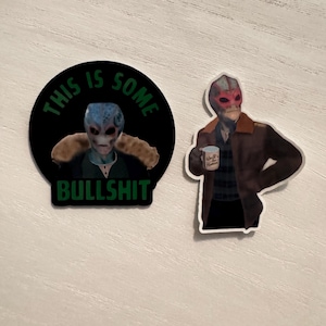 May include: Two stickers featuring an alien design. One is a black circle with the text "THIS IS SOME BULLSHIT" around an alien image. The other sticker shows an alien holding a mug that says "World Hunter".