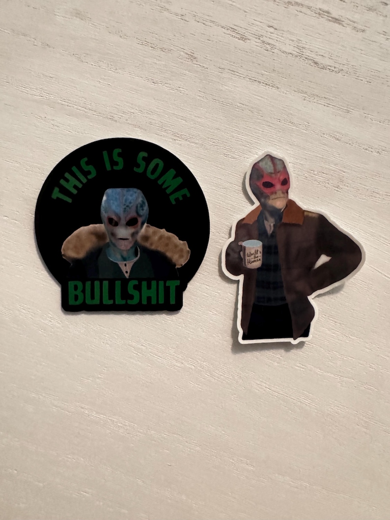 May include: Two stickers featuring an alien design. One is a black circle with the text "THIS IS SOME BULLSHIT" around an alien image. The other sticker shows an alien holding a mug that says "World Hunter".